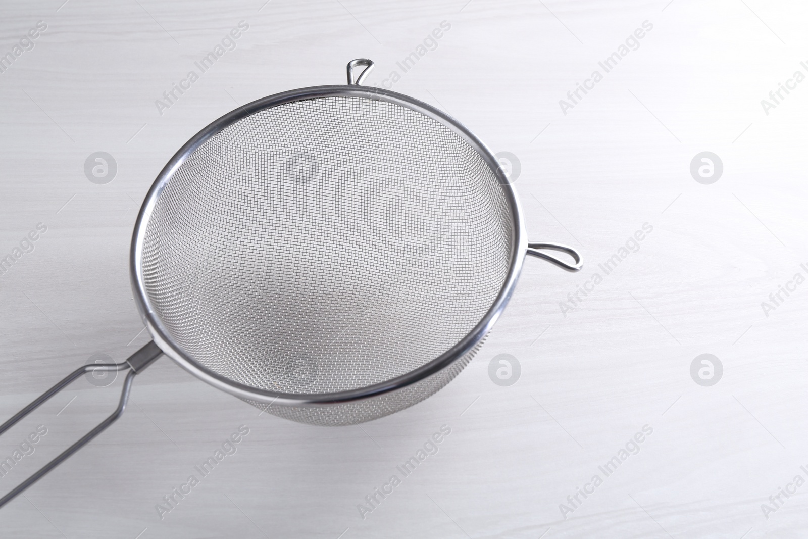 Photo of One metal sieve on white wooden table. Space for text