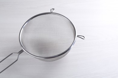 Photo of One metal sieve on white wooden table. Space for text