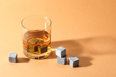 Photo of Whiskey stones and drink in glass on orange table. Space for text