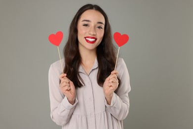 Beautiful young woman with paper hearts on grey background