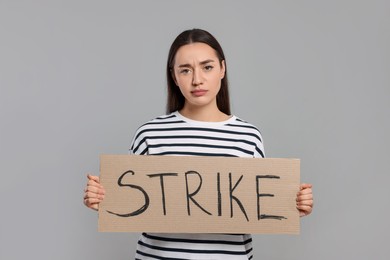 Photo of Upset young woman holding cardboard banner with word Strike on light grey background