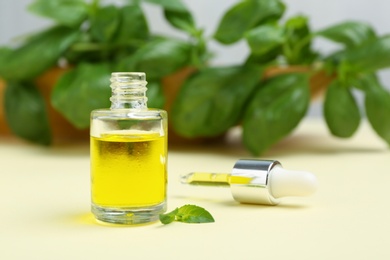 Photo of Glass bottle with basil oil, leaves and dropper on table