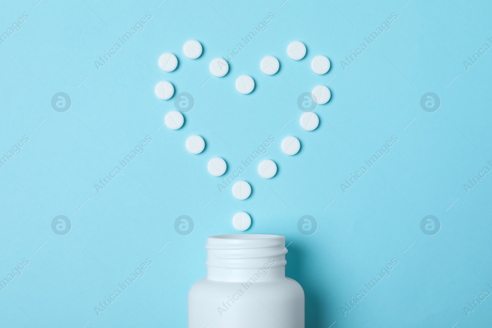 Photo of Heart made of pills and container on color background, top view. Cardiology concept