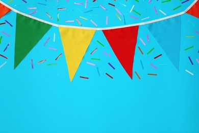 Bunting with colorful triangular flags and confetti on light blue background, flat lay. Space for text