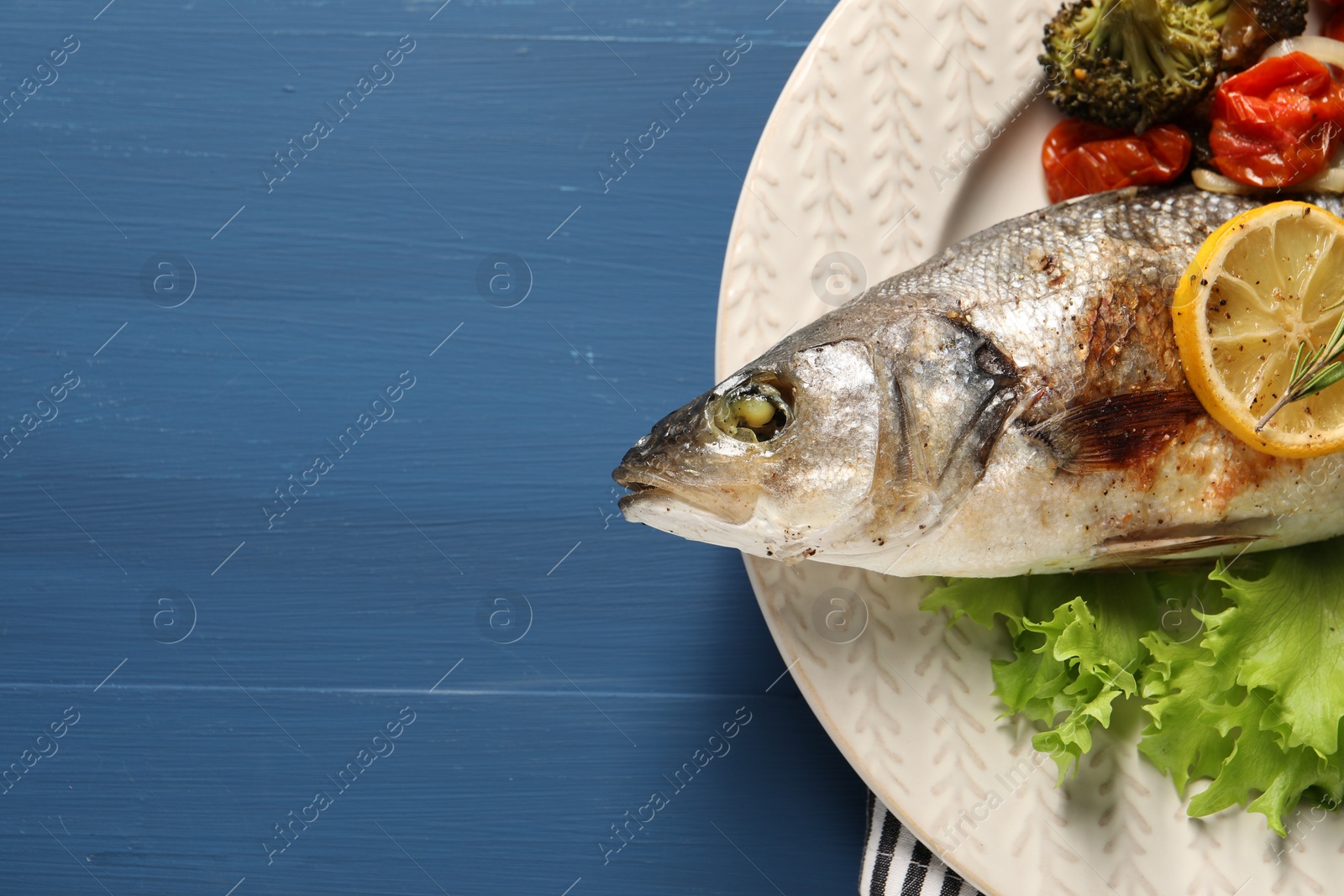 Photo of Delicious baked fish and vegetables on blue wooden table, top view. Space for text