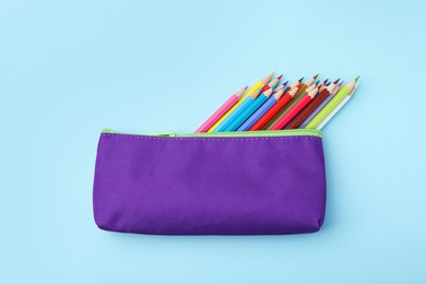 Photo of Many colorful pencils in pencil case on light blue background, top view