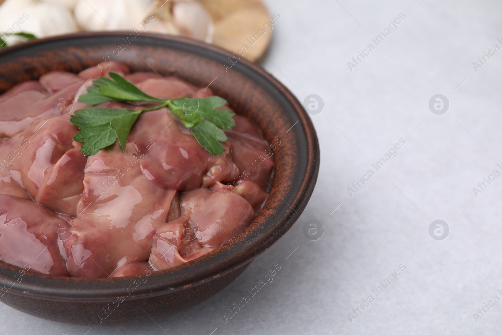 Photo of Bowl with raw chicken liver and parsley on white table, closeup. Space for text