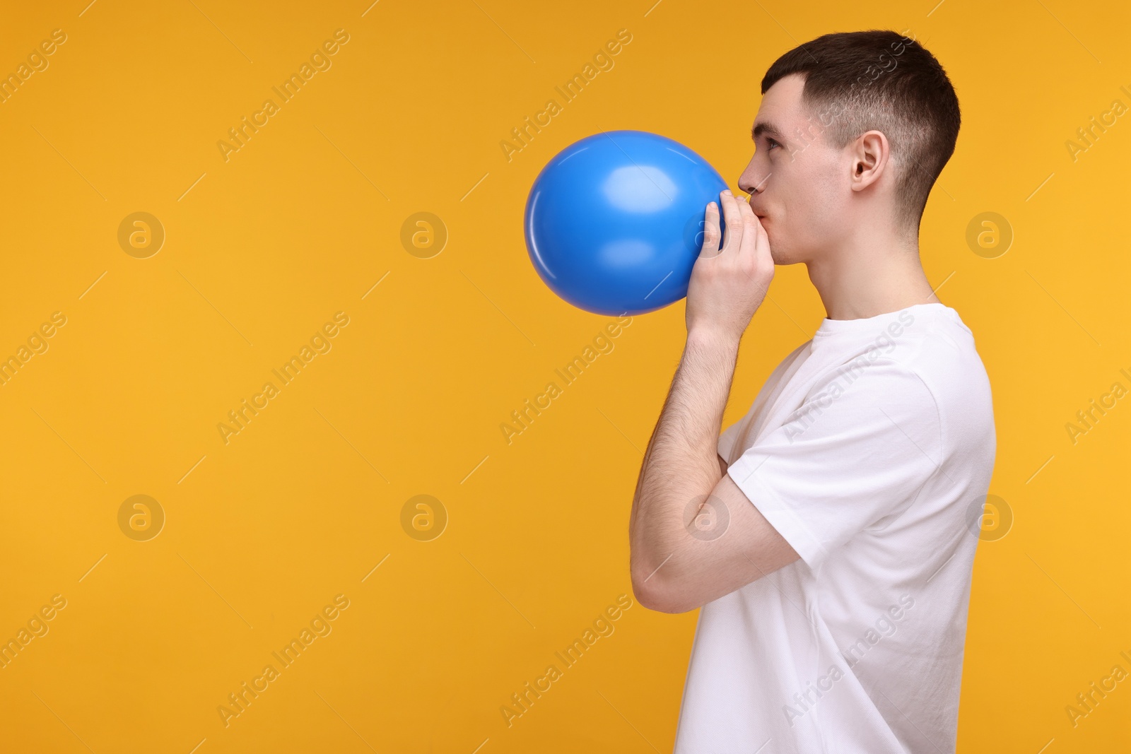 Photo of Young man inflating light blue balloon on yellow background. Space for text