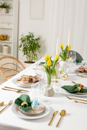 Photo of Festive Easter table setting with painted eggs, candles and yellow tulips in room