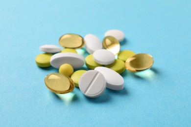 Pile of different pills on light blue background, closeup