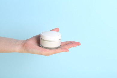 Woman with jar of cream on light blue background, closeup