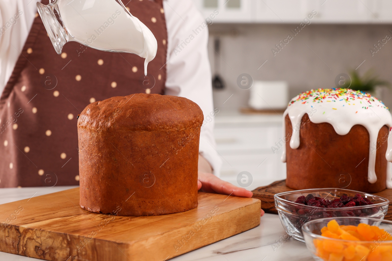 Photo of Woman decorating traditional Easter cake with glaze at white marble table in kitchen, closeup