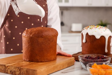 Woman decorating traditional Easter cake with glaze at white marble table in kitchen, closeup