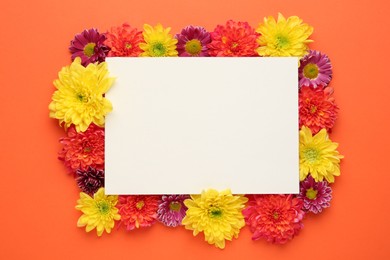 Photo of Frame made of beautiful chrysanthemum flowers and blank card on orange background, flat lay. Space for text