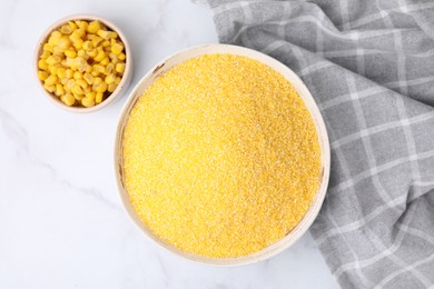 Photo of Raw cornmeal and corn kernels in bowls on white marble table, top view