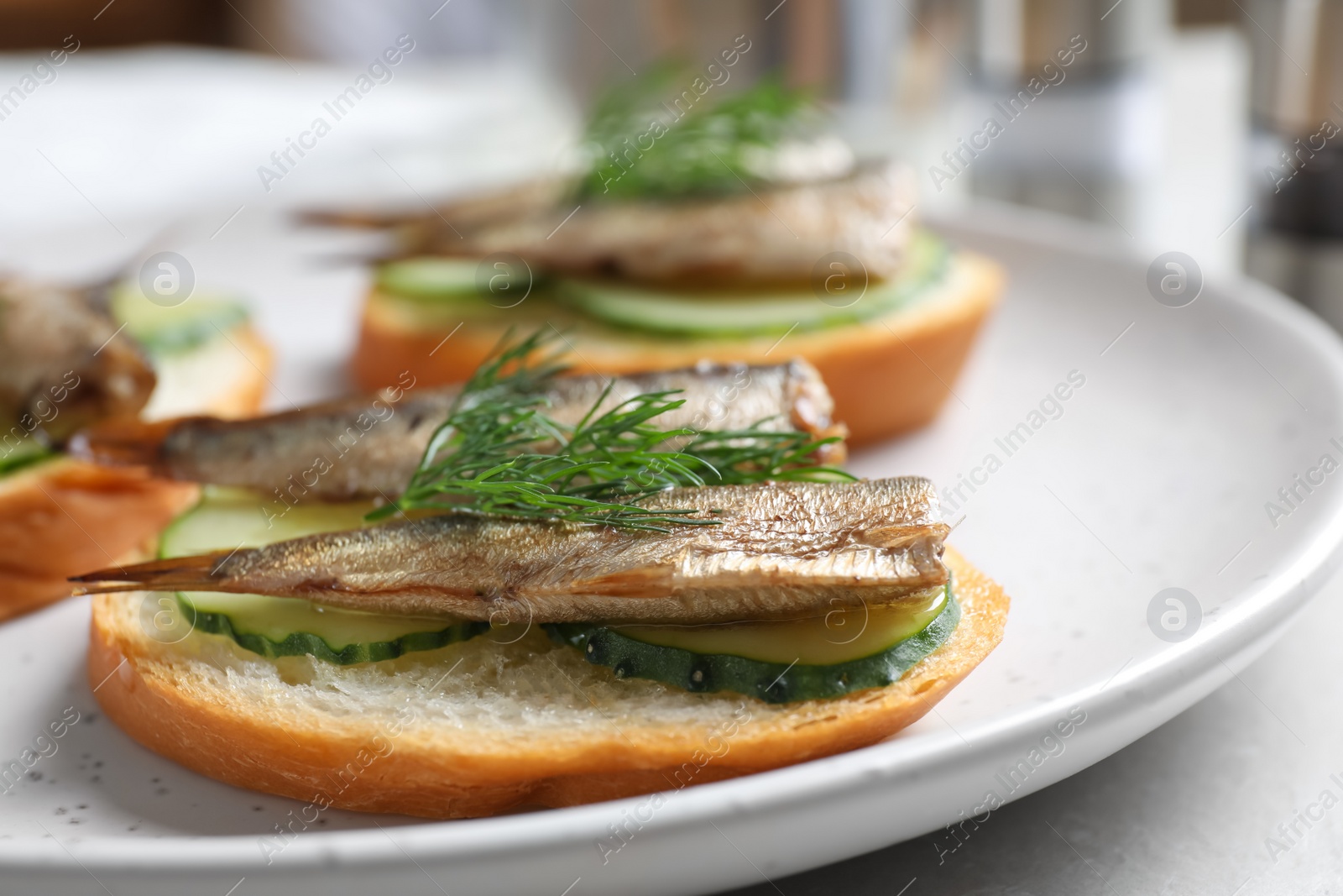 Photo of Delicious sandwiches with sprats, cucumbers and dill on plate, closeup