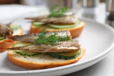 Delicious sandwiches with sprats, cucumbers and dill on plate, closeup