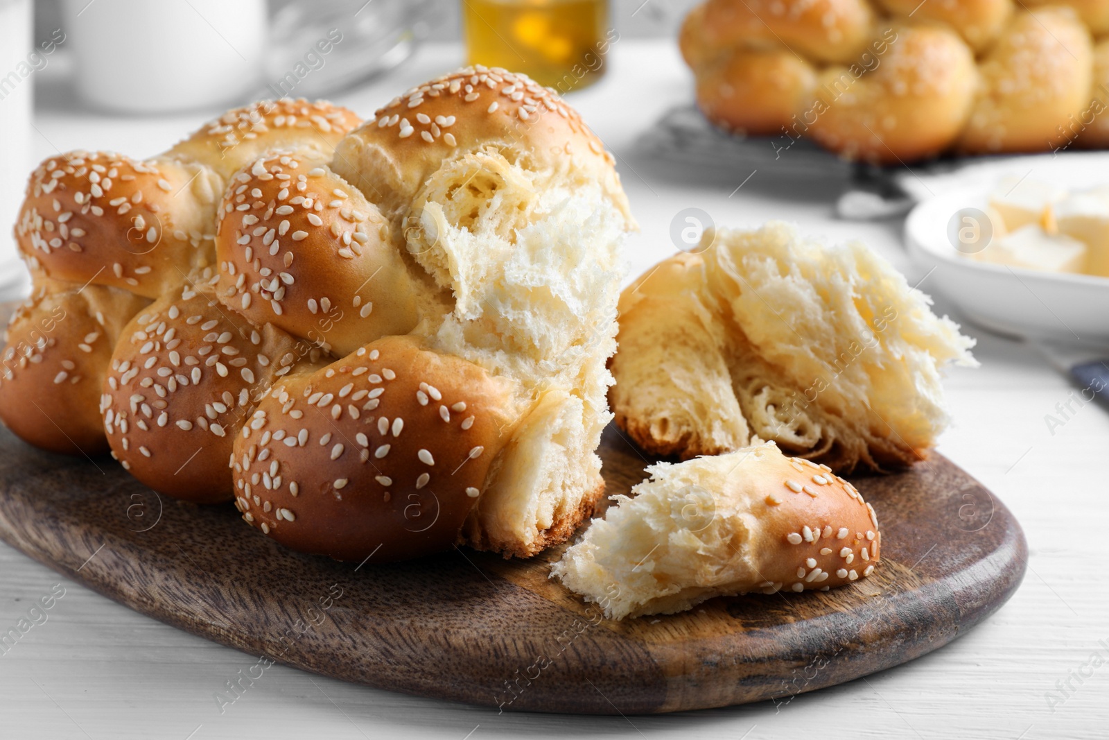 Photo of Homemade braided bread with sesame seeds on white wooden table, closeup. Traditional challah