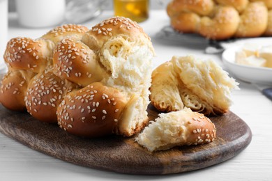 Photo of Homemade braided bread with sesame seeds on white wooden table, closeup. Traditional challah