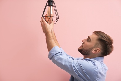 Man changing light bulb in lamp on color background