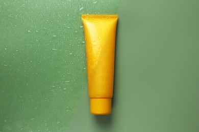 Tube with moisturizing cream on wet green surface, top view