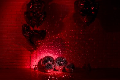 Photo of Many shiny disco balls in room decorated with heart shaped balloons, toned in red