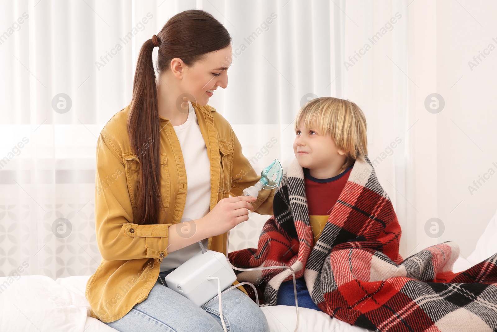 Photo of Mother helping her sick son with nebulizer inhalation in bedroom