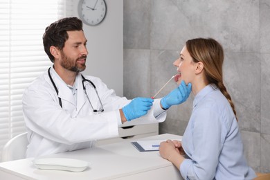 Photo of Doctor taking throat swab sample from woman`s oral cavity indoors