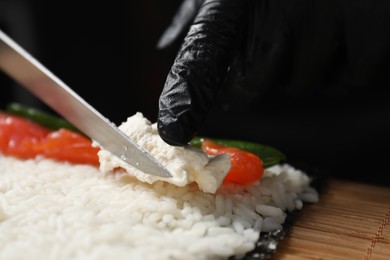 Chef in gloves putting cream cheese onto unwrapped sushi roll at table, closeup