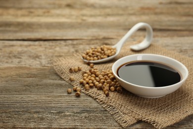 Photo of Soy sauce in bowl and beans on wooden table. Space for text