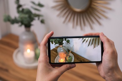 Photo of Woman taking photo of stylish interior accessories on wooden table with smartphone, closeup
