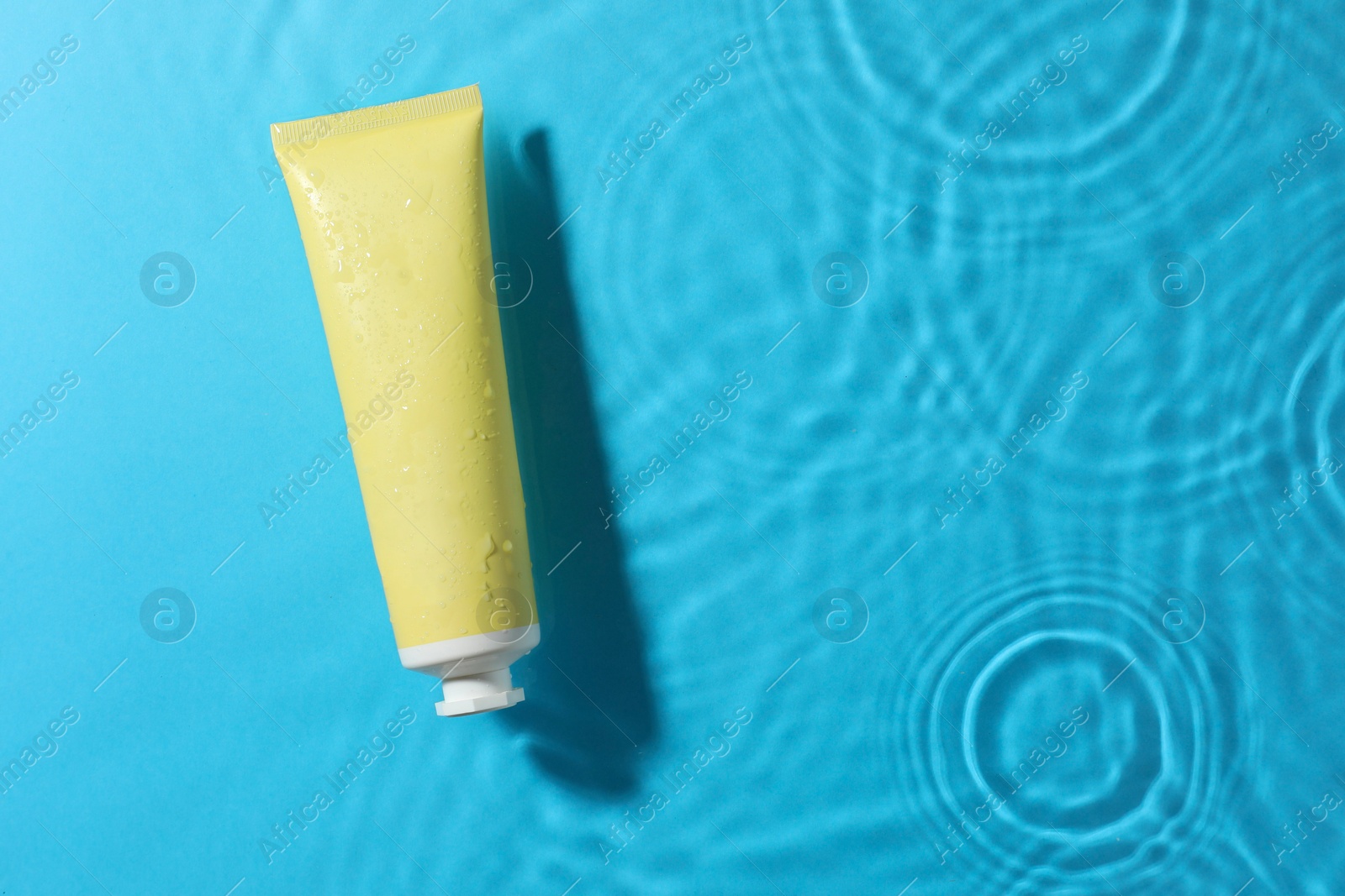 Photo of Tube with moisturizing cream in water on light blue background, top view. Space for text