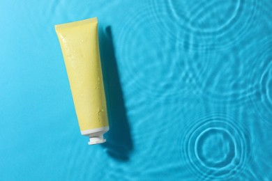 Photo of Tube with moisturizing cream in water on light blue background, top view. Space for text