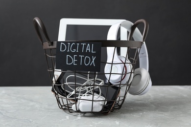 Photo of Trash bin with different gadgets and words DIGITAL DETOX on light grey marble table