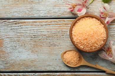 Orange sea salt in bowl, flowers and spoon on wooden table, flat lay. Space for text