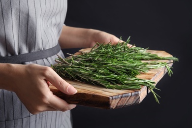 Photo of Woman holding wooden board with fresh rosemary twigs on black background, closeup