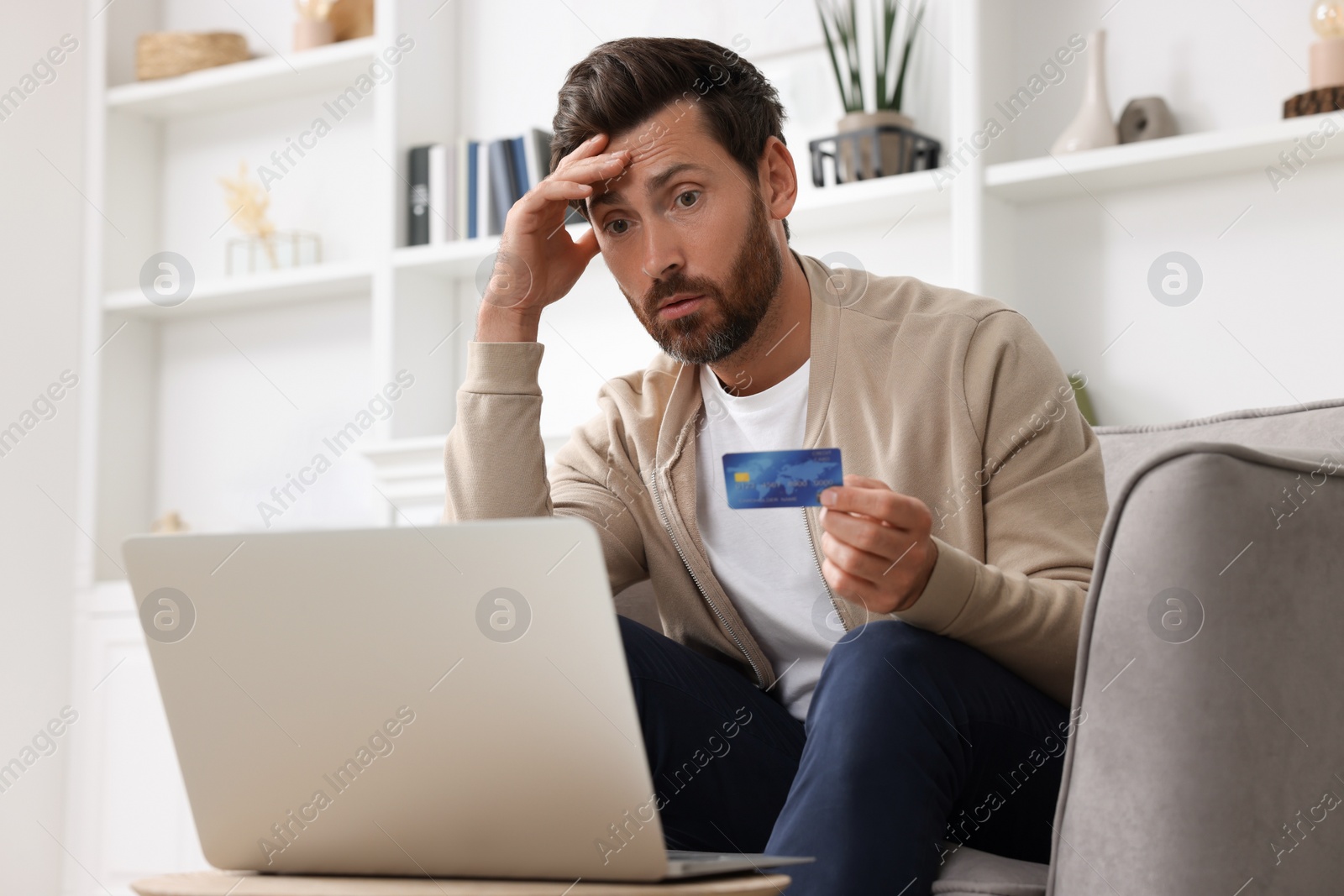 Photo of Upset man with credit card near laptop at home. Be careful - fraud