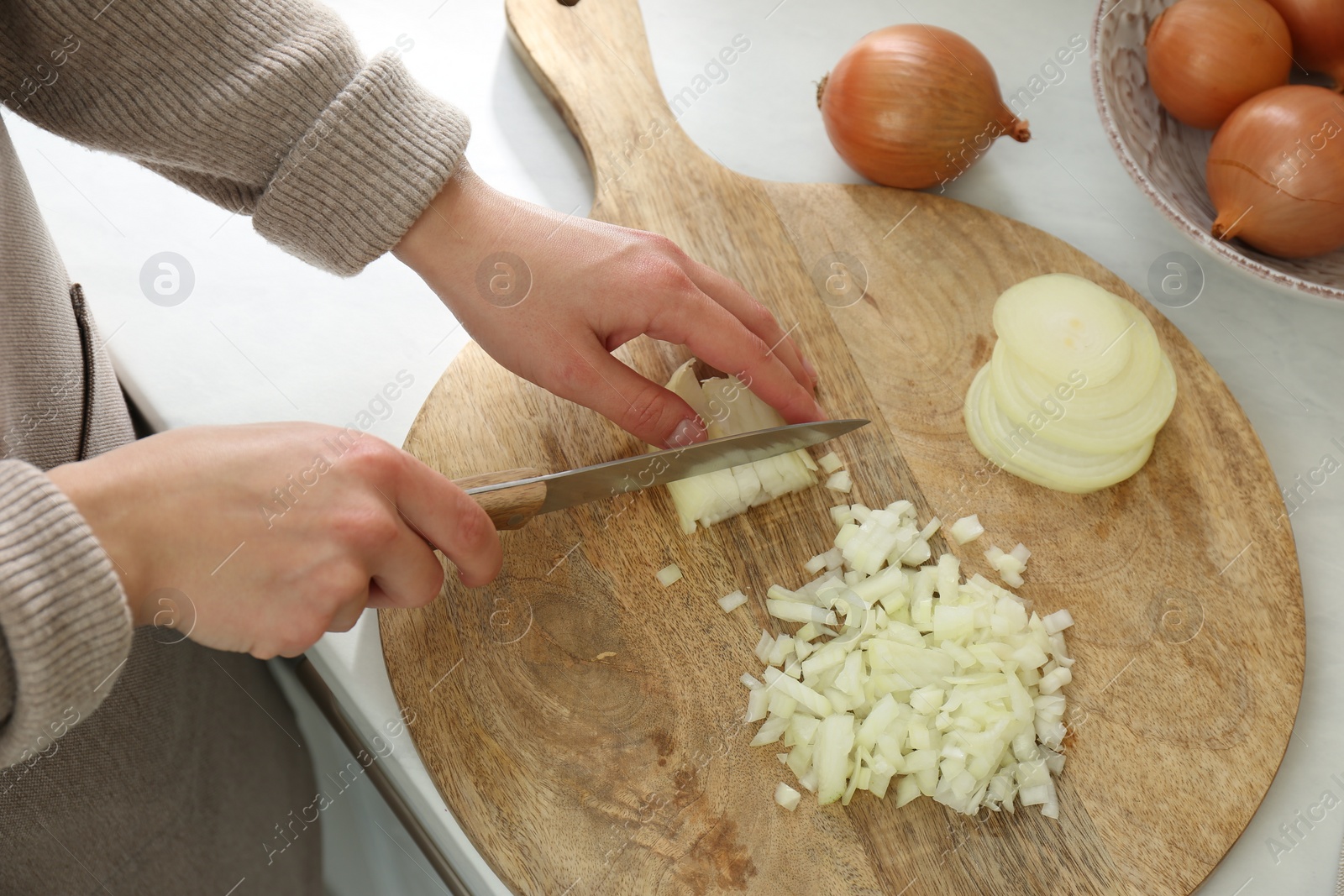 Photo of Woman chopping white onion on wooden board at table, closeup