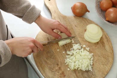 Photo of Woman chopping white onion on wooden board at table, closeup