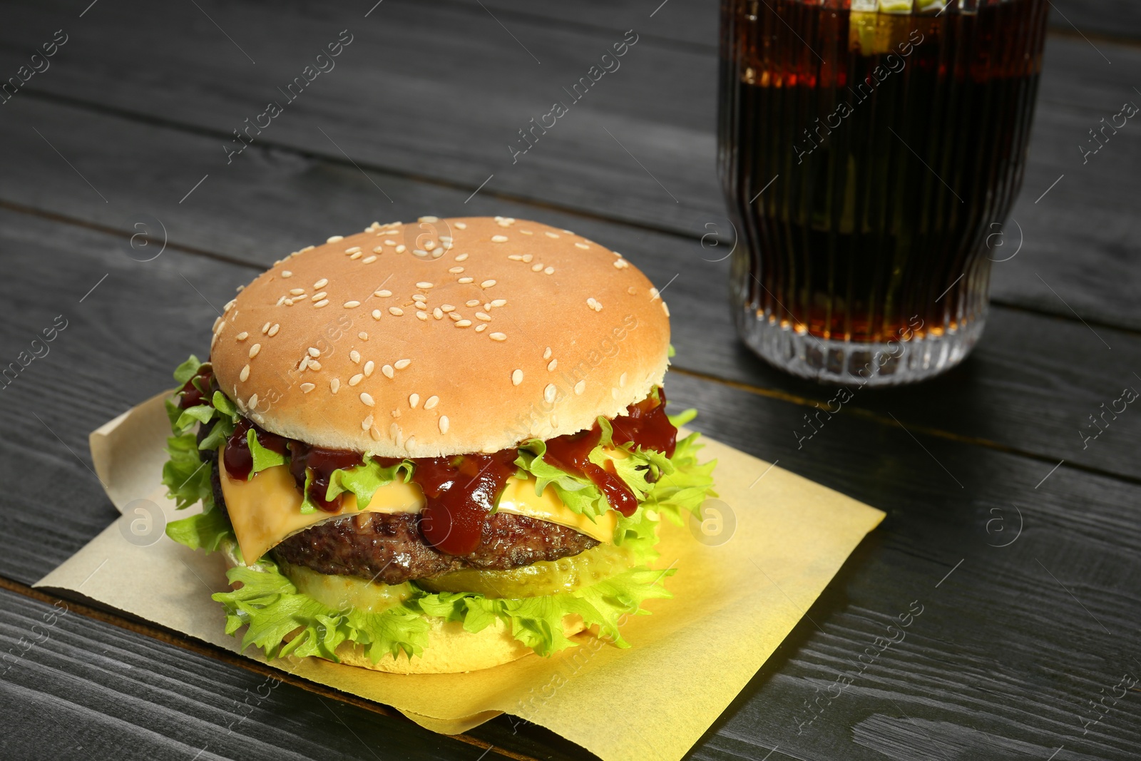 Photo of Burger with delicious patty and soda drink on black wooden table