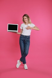 Young woman with modern laptop on pink background