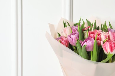 Photo of Bouquet of beautiful tulips near white wall, closeup. Space for text