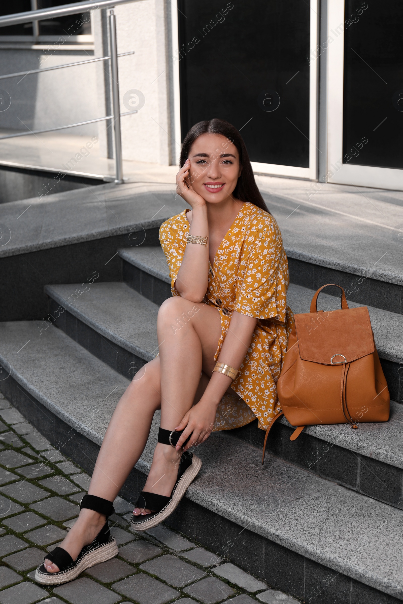 Photo of Beautiful young woman with stylish backpack sitting on stairs outdoors