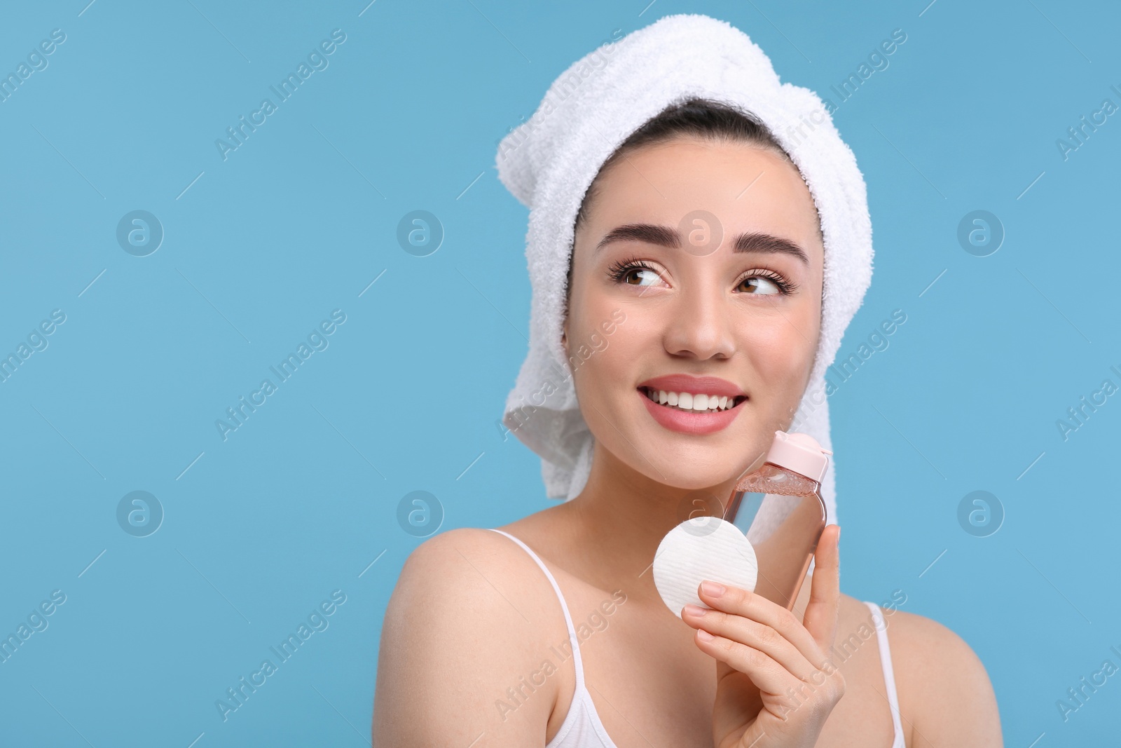 Photo of Beautiful woman with makeup remover and cotton pad on light blue background, space for text