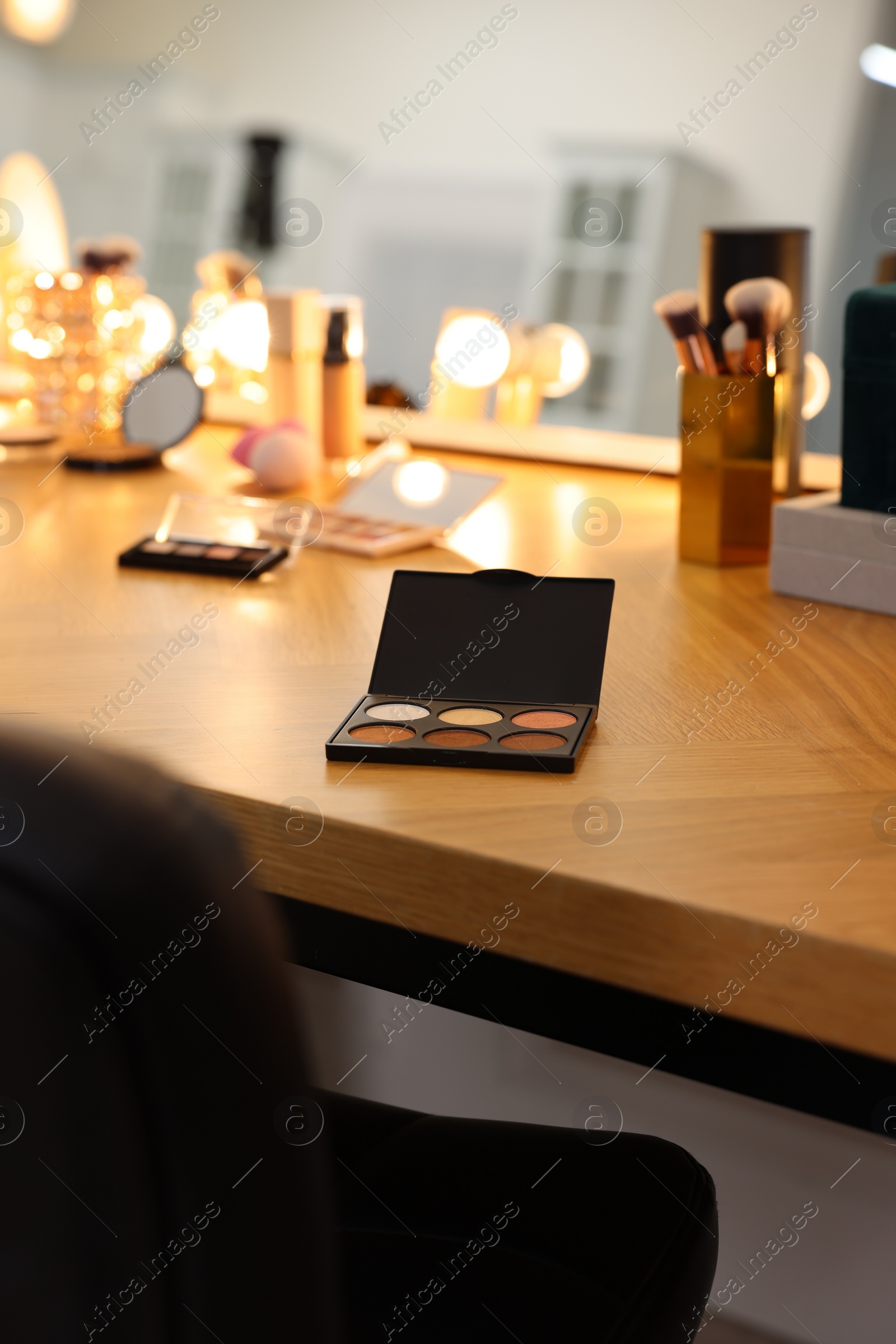 Photo of Eyeshadow palette and other cosmetic products on wooden dressing table in makeup room