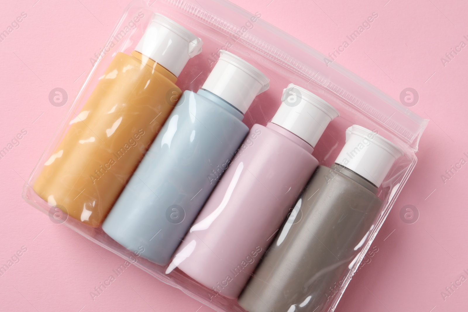 Photo of Cosmetic travel kit in plastic bag on pink background, top view. Bath accessories