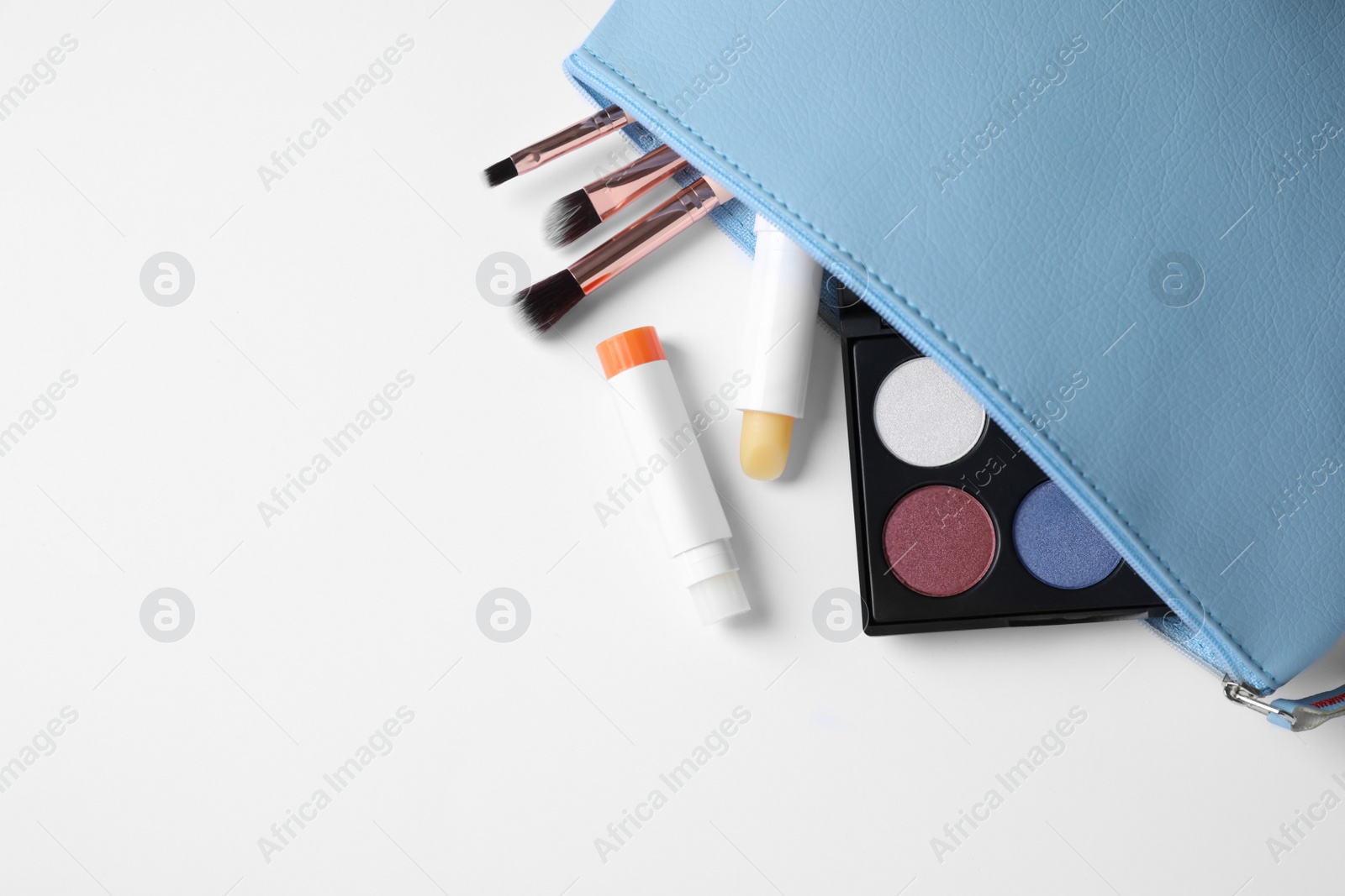 Photo of Bag with hygienic lipsticks and cosmetic products on white background, top view