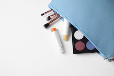 Bag with hygienic lipsticks and cosmetic products on white background, top view