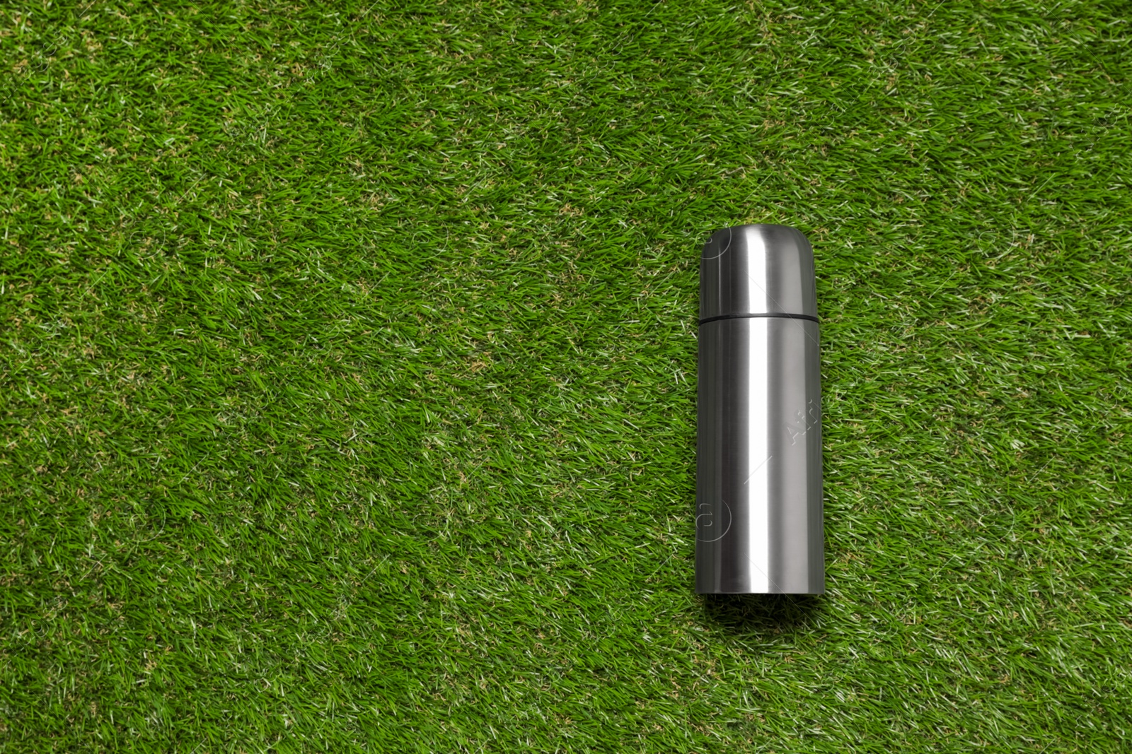 Photo of Modern silver thermos on green grass, top view. Space for text