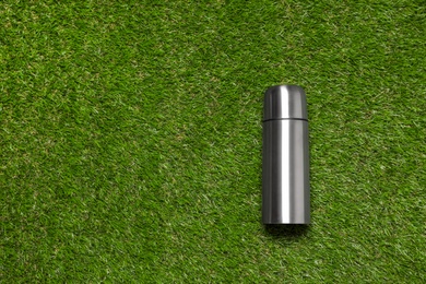 Photo of Modern silver thermos on green grass, top view. Space for text